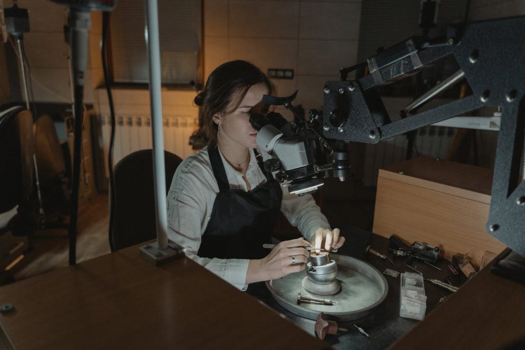 A woman jeweler crafting intricate pieces with precision under a microscope in a workshop.
